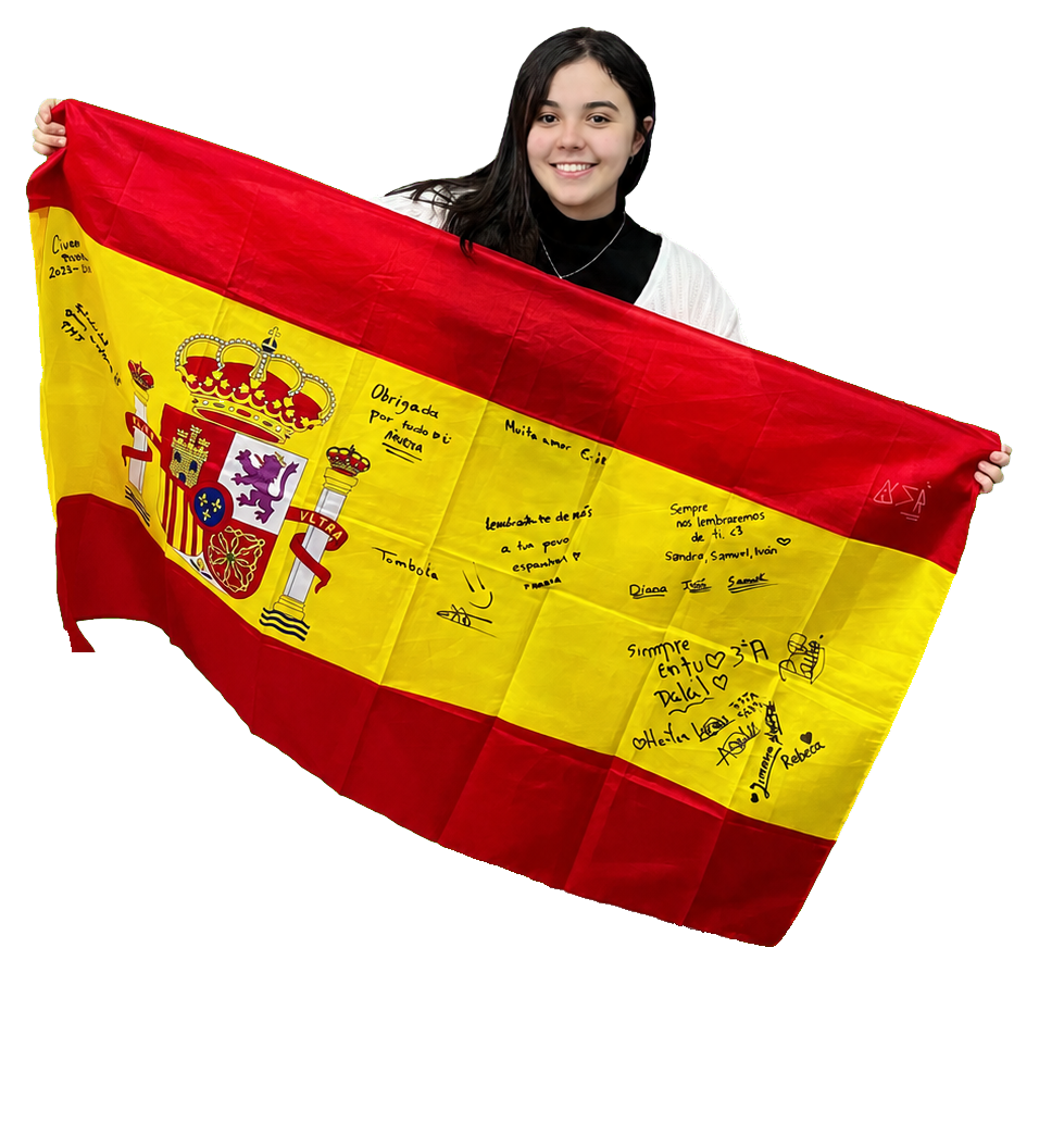 Professora Giu sorrindo e segurando uma bandeira da Espanha autografada por seus alunos